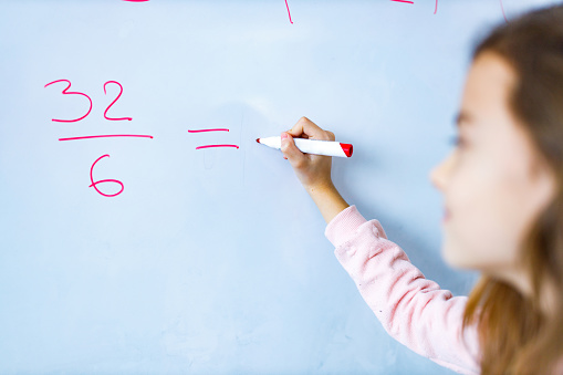 Close-up of girl writing mathematics on whiteboard in the classroom