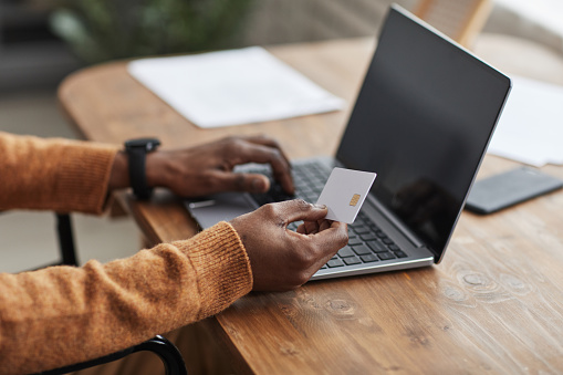 Close up of unrecognizable African-American man holding mockup credit card while online shopping via laptop, copy space