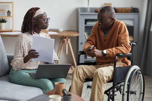 African-American Wheelchair User Talking to Business Consultant Portrait of African-American couple with handicapped man using wheelchair working from home together in modern interior social services stock pictures, royalty-free photos & images