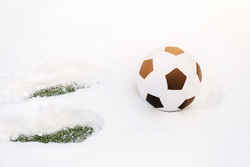 Classic soccer ball on a snowy sports ground and footprints in the snow.