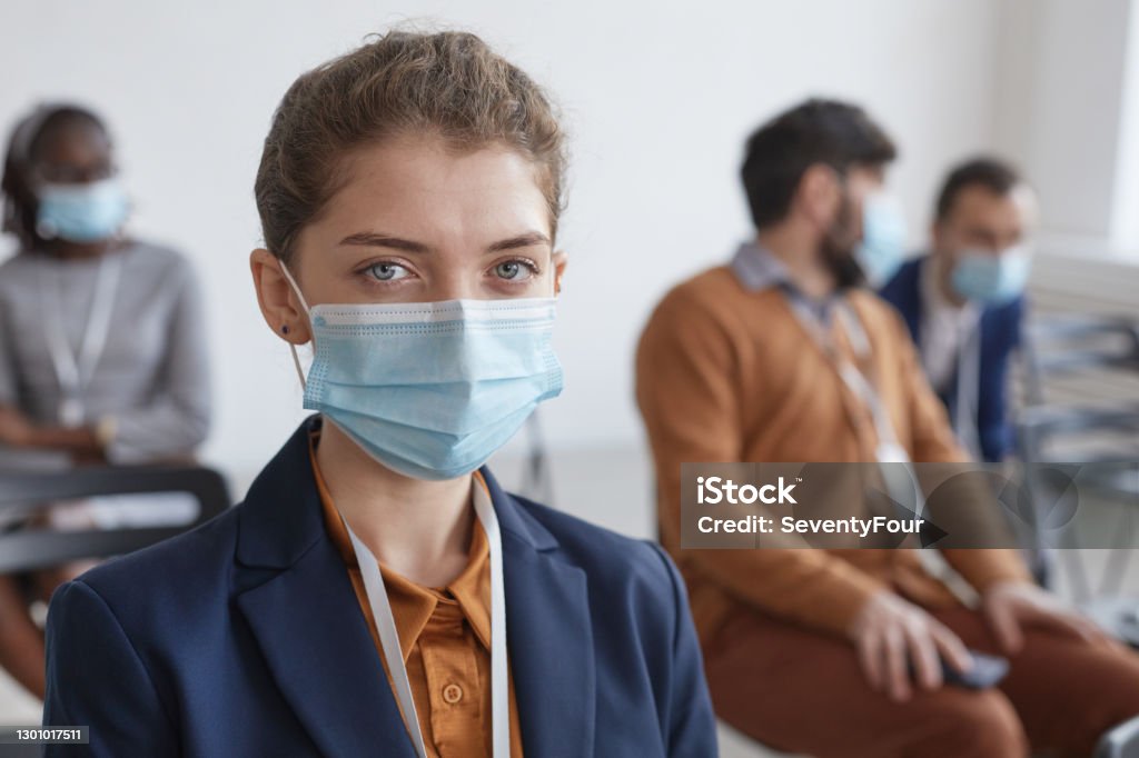 Young Woman Wearing Mask in Audience Front view portrait of young businesswoman wearing mask and looking at camera while sitting in audience at business conference or seminar, copy space Protective Face Mask Stock Photo