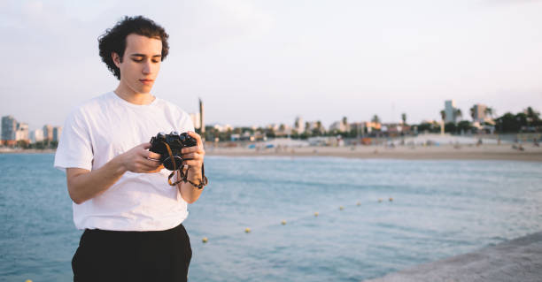 istock Hipster guy looking at photo camera on waterfront 1301019424
