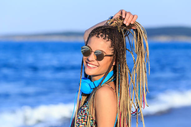 Cheerful young girl with braided hair and headphones having fun on beach.