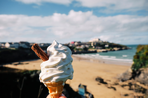 POV of a hand holding a melting ice cream overlooking Towan Beach, Newquay, Cornwall on a bright Sunny Autumn day.