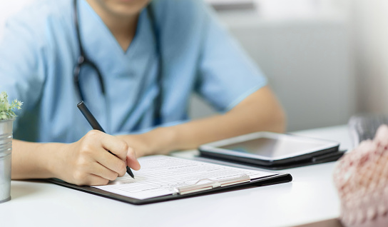Asian Female Doctor or nurse in blue uniform working and writing on clipboard or paperwork or prescription in hospital.