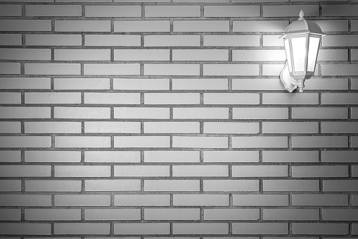 Light brick wall texture background with white lantern with light on. Copy space for text. Spain.