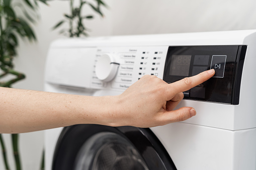 Selective focus on cropped woman hand select settings for laundry on modern digital display. Close up view of automatic washing machine with touch screen on control panel. Female press start or pause