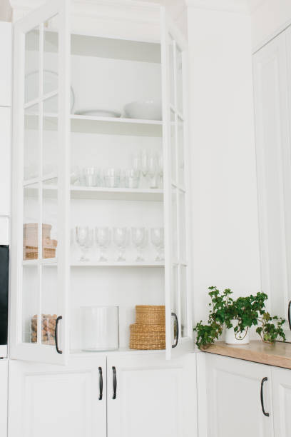 istock Opened white glass cabinet with clean dishes and decor. Scandinavian style kitchen interior. Organization of storage in kitchen. Vertical photo. 1301030753
