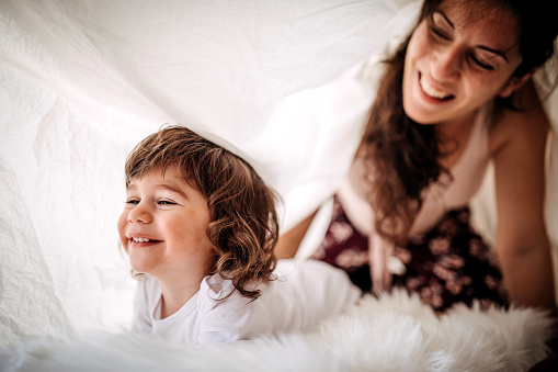 Mother and son having fun in bedroom under the blanket