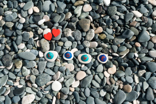 Beach stones background with two red hearts and a word Love written on painted seashells