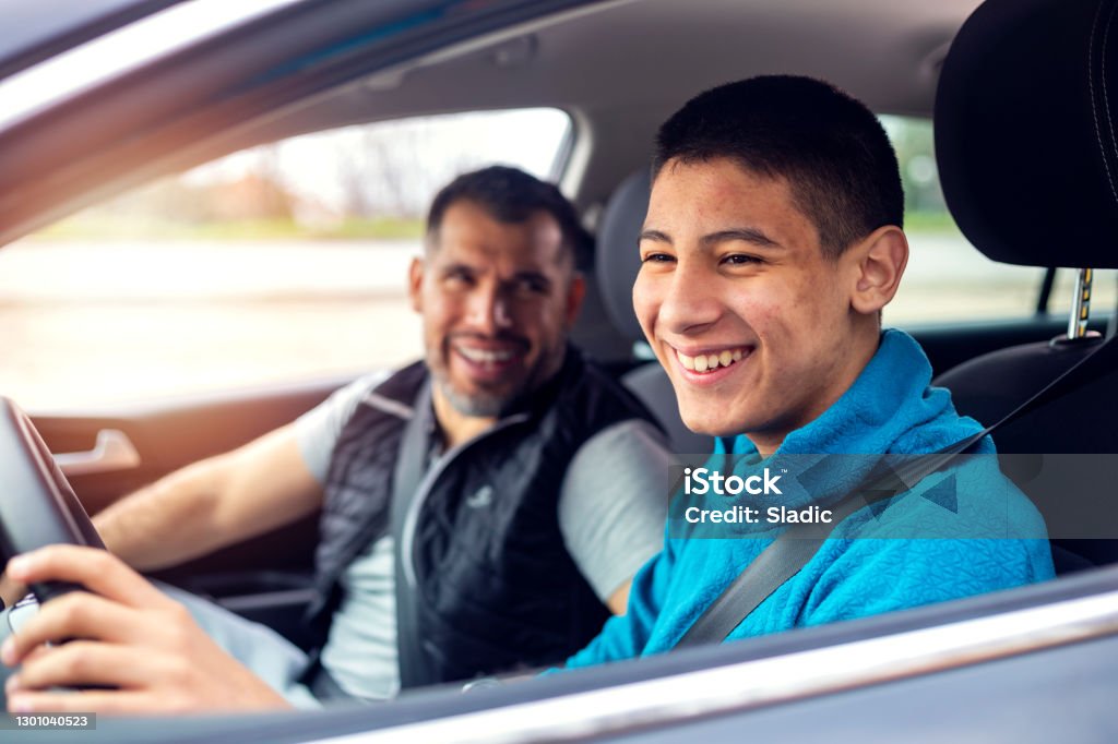 Teenage boy having driving lesson with male instructor A teenage boy sitting behind the steering wheel of a car and listening to his fathers instructions as he drives. Teenager Stock Photo