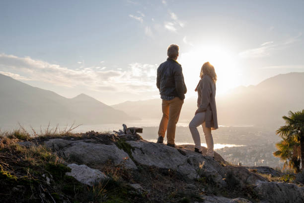 caminata pareja madura a lo largo de la cresta soleada de la montaña, puesta de sol - pertenencias fotografías e imágenes de stock