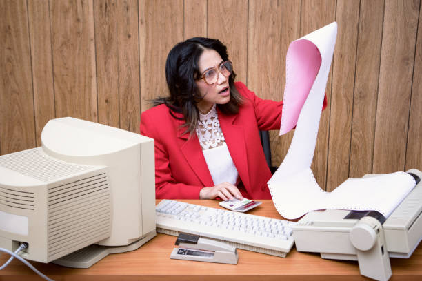 Retro Secretary At Computer Desk In Vintage Office A vintage Filipino business woman at the office works at an old computer at her desk.  1980's - 1990's fashion style.  Wood paneling on wall in the background. overworked funny stock pictures, royalty-free photos & images