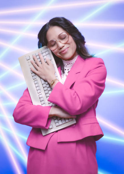 Retro Office Worker Portrait With Laser Background A portrait of a vintage Filipino business woman in retro style, hugging a computer keyboard.  Glamour shot type portrait.  1980's - 1990's fashion style. 1990s style stock pictures, royalty-free photos & images
