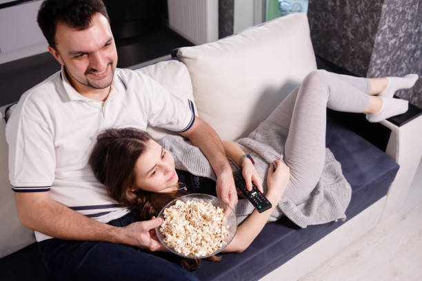 istock Young couple eating popcorn while watching movie lying on sofa 1301043435