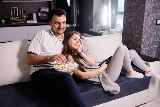 istock Young couple eating popcorn while watching movie lying on sofa 1301043442