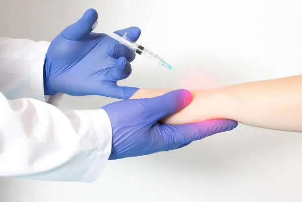 Photo of A doctor rheumatologist performs a wrist block on a patient who has pain and inflammation in the joint. Concept of injections with local anesthetic and chondroprotectors, close-up