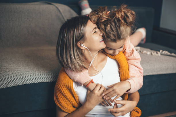 caucasian daughter embracing her mom while she is listening music on earphones and smile - babies and children audio imagens e fotografias de stock