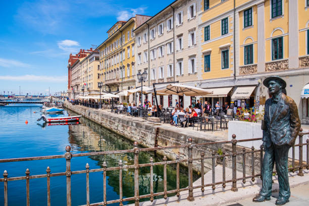 Trieste, Canal Grande of Trieste (Friuli-Venezia Giulia, Italy) People relaxing on the banks of the Canal Grande of Trieste, a large navigable canal built in 1754-1756 in the center of the city. The statue of James Joyce stands on the Ponte Rosso since 2004, created by the Trieste sculptor Nino Spagnoli on the centenary of Joyce's arrival in Trieste. trieste stock pictures, royalty-free photos & images