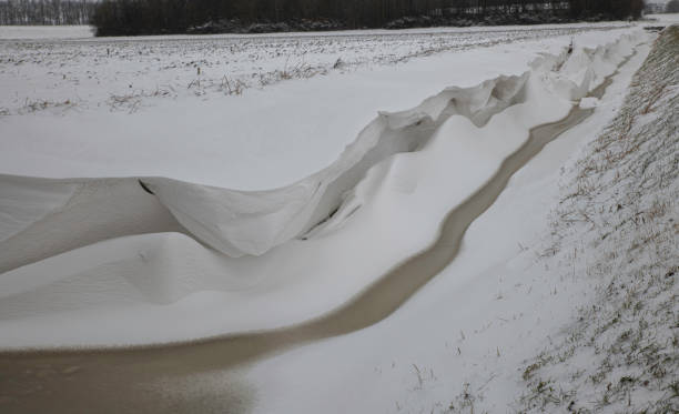 una gruesa capa de nieve que sobresale de una zanja casi congelada - thick snow fotografías e imágenes de stock