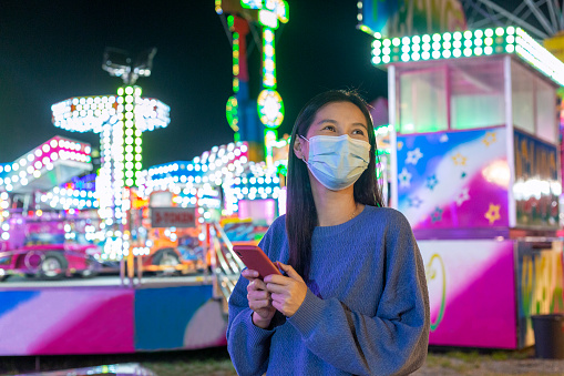 New normal after covid - Asian woman wearing protective face mask while visiting amusement park at night