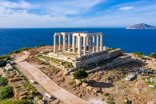 Cape Sounio, Greece. Poseidon temple aerial drone view. Archaeological site of ancient greek ruins up on a hill, Athens Attica. Cloudy blue sky backgrpund, sunny day