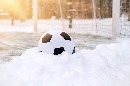 Soccer ball placed on snowdrift near goal in winter on sports ground, sunny day
