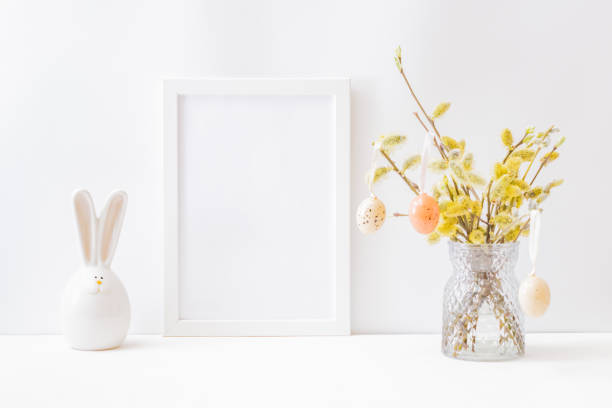 istock Home interior with easter decor. Mockup with a white frame and willow branches in a vase on a light background 1301056967
