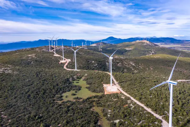 Wind farm, Wind turbines and curvy road on the hill, aerial drone view, Green ecological power energy generation. Alternative energy plant, blue cloudy sky,