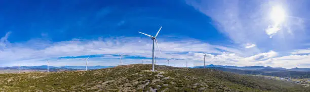 Wind turbines on the hill. Wind farm panorama. Green ecological power energy generation. Alternative energy plant, sun shining on blue cloudy sky, Greece