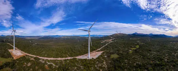 Wind turbines and curvy road on the hill. Wind farm panorama, aerial drone view. Green alternative ecological power energy generation, blue cloudy sky, sunny day, Greece