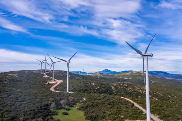 Wind farm, Wind turbines and curvy road on the hill, Green ecological power energy generation. Alternative energy plant, blue cloudy sky, sunny day, Greece