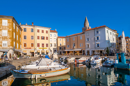 People relaxing in a summer late afternoon in the old town of Muggia, next to the little harbor where yachts and fishing boats are moored.