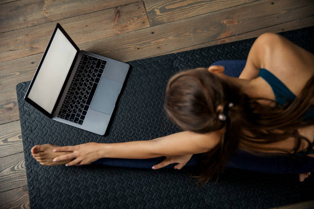 istock Female practicing yoga or pilates indoors on mat, doing exercises and stretching, watching video lesson online. Top view 1301059997