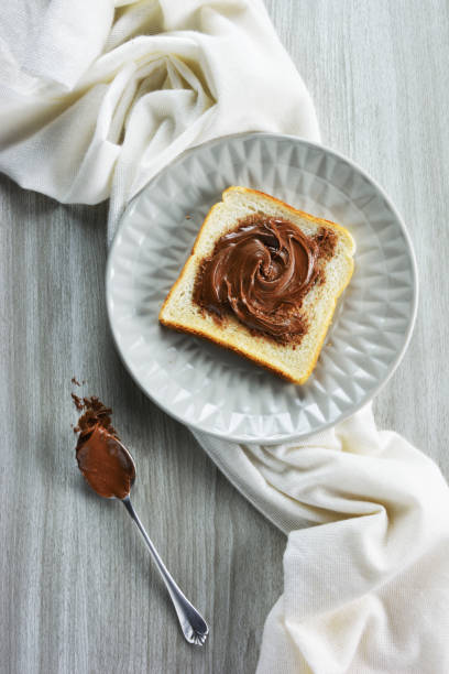 istock Slice of bread spread with hazelnut praline paste on  a plate  and a spoon besides 1301061319