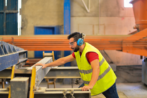 Bearded man working in factory with glasses and ear protection.