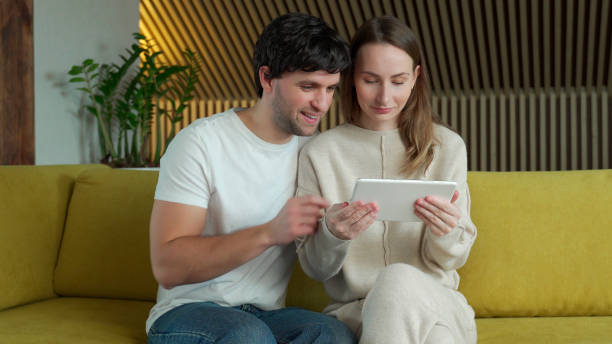istock Young couple watching media content online in a tablet sitting on a sofa at home 1301062518