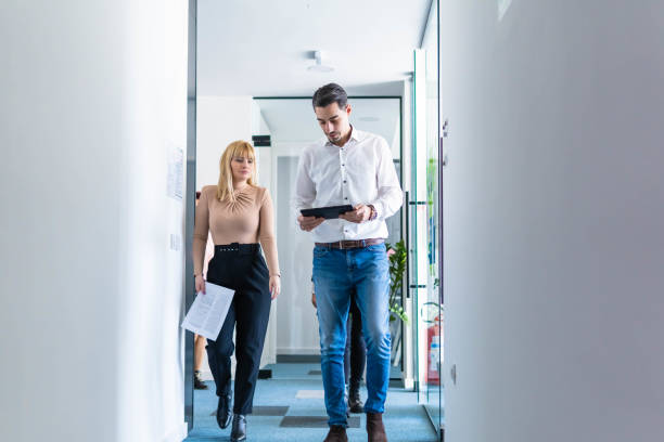 istock Male and female colleagues at work walking through a hallway holding a digital tablet 1301068498