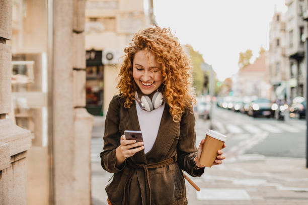 istock Young woman is using mobile phone on the move and holing reusable coffee cup 1301073545