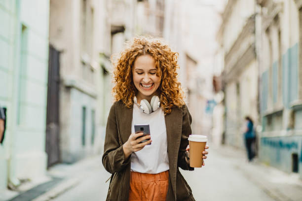 istock Young woman is using mobile phone on the move and holing reusable coffee cup 1301073705