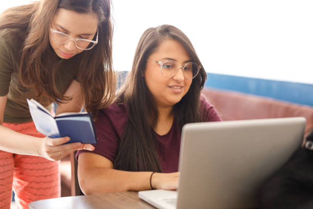 istock Smiling young woman using laptop while her girlfriend holds a passport 1301076383