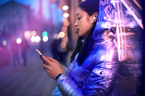 fille à la mode d’adolescent utilisant le smartphone, restant dans la lumière rougeoyante de néon - human settlement audio photos et images de collection