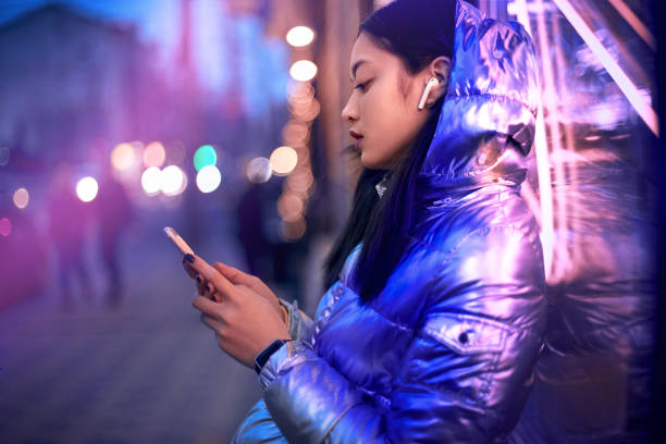 Trendy teenager girl using smartphone, standing in glowing neon light stock photo