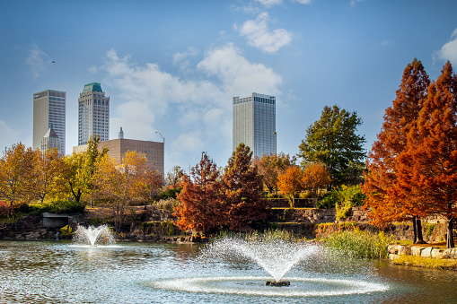 11-16 2020 - Tulsa USA - View from Central Park of downtown Tulsa Oklahoma on bright autumn day with colorful foliage and lake and fountains in foreground and vintage skyscrapers behind