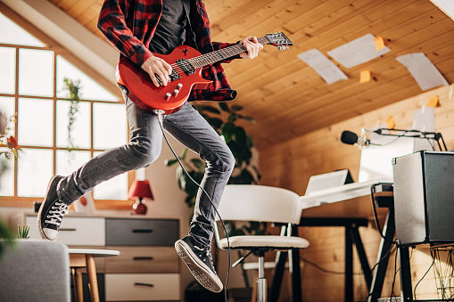 One man, teenage male guitarist having fun playing music on electric guitar in living room at home.