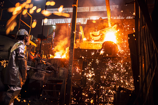 Trabajador de fundición controlando el proceso de derretimiento de hierro en el horno. Quema de acero líquido vertiendo y chispas volando por todas partes. Metalurgia e industria pesada. photo
