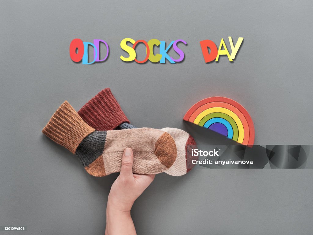 Odd Socks Day. Hand hold pair of mismatched socks. Wooden rainbow, toy figures. Social initiative against bullying in school or workplace. Promotion design for anti-bullying campaign Odd Socks Day. Hand hold pair of mismatched socks. Wooden rainbow, toy figures. Social initiative against bullying in school or workplace. Design for anti-bullying campaign promotion poster. Flat Lay Stock Photo
