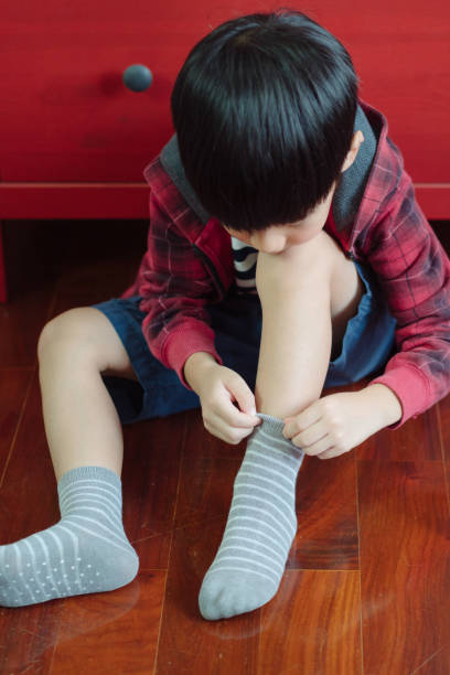 istock Cute Asian boy getting dressed for school, putting on socks, smiling with happiness to go back to school 1301102896