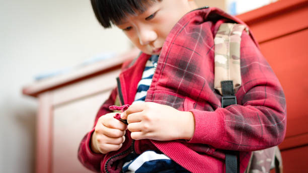 かわいいアジアの男の子は、学校のために服を着て、下を見て、ジャケットをジップアップし、学校に戻る準備をしなさい - taking off ストックフォトと画像