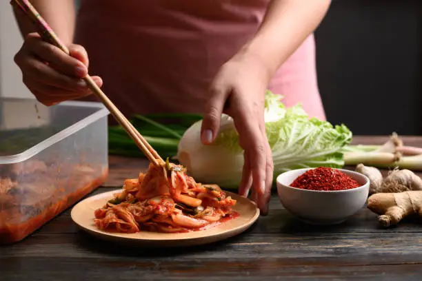 Woman hand picking kimchi cabbage by chopsticks on wooden plate for eating, Homemade Korean food